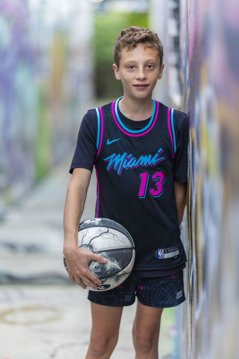 Boy in a Miami basketball jersey against a colorful mural
