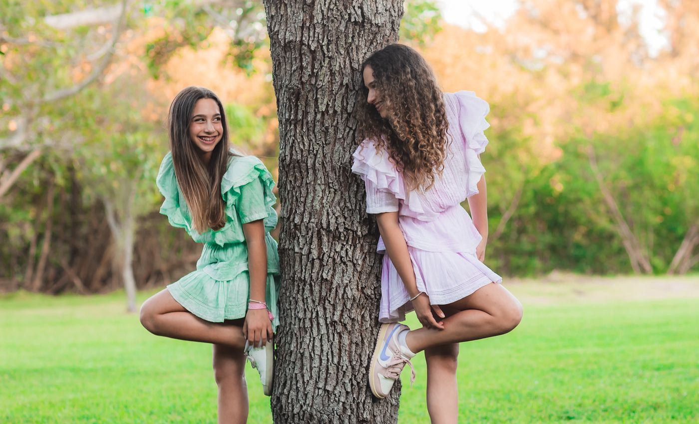 Two girls in matching dresses leaning against a tree
