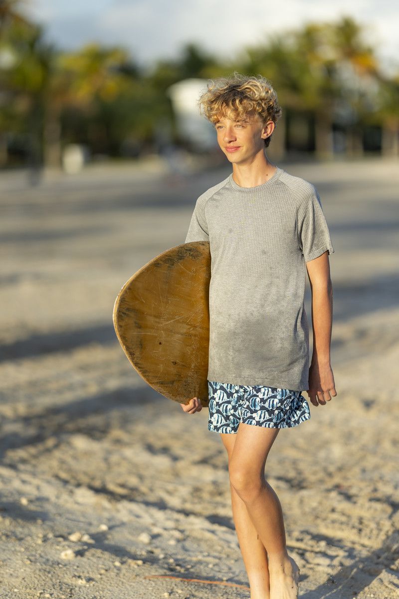 Boy walking the beach with a skimboard