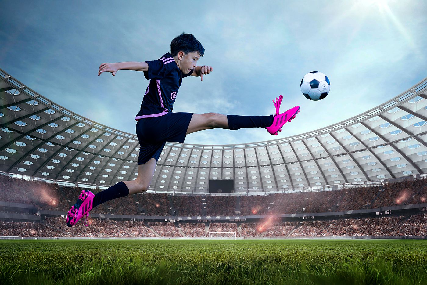 Boy in a soccer kit striking a ball in a floodlit stadium