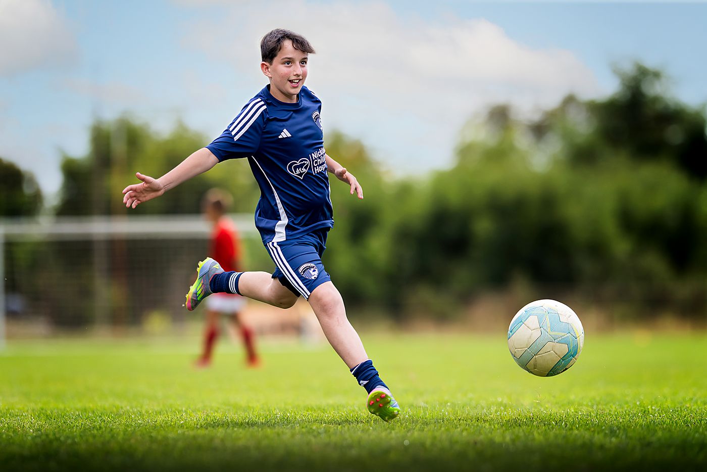Boy in a blue kit running onto the ball on a grass pitch