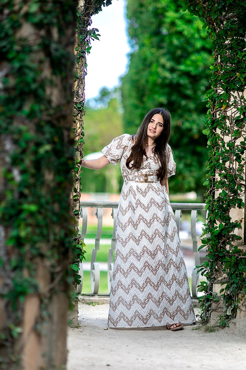 Girl in a long patterned dress framed by a leafy garden archway