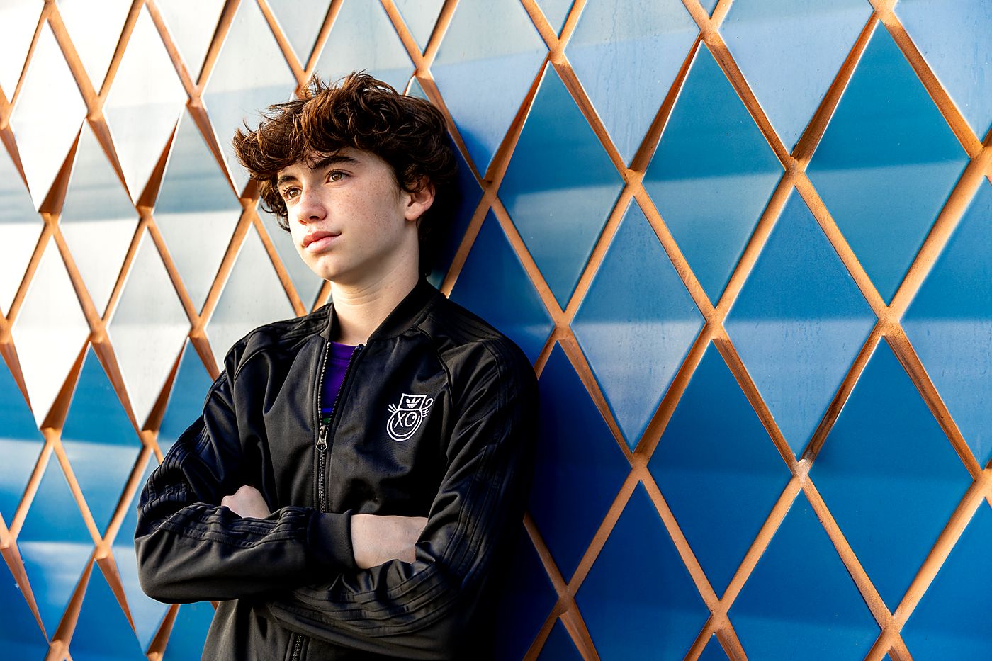 Boy in a varsity jacket against a blue and gold lattice wall