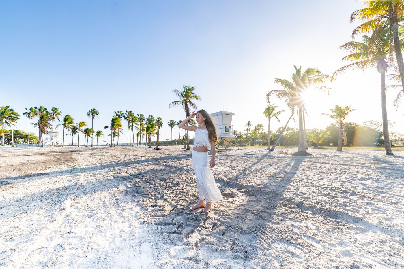 Girl walking on the beach among palm trees at sunrise