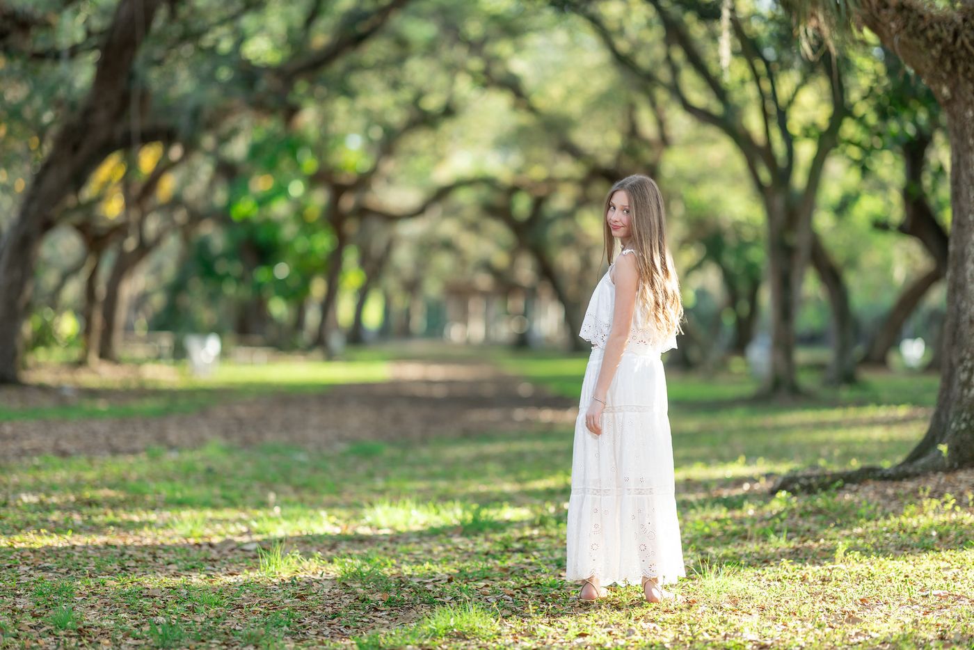 Girl in a white dress walking a tree-lined nature trail